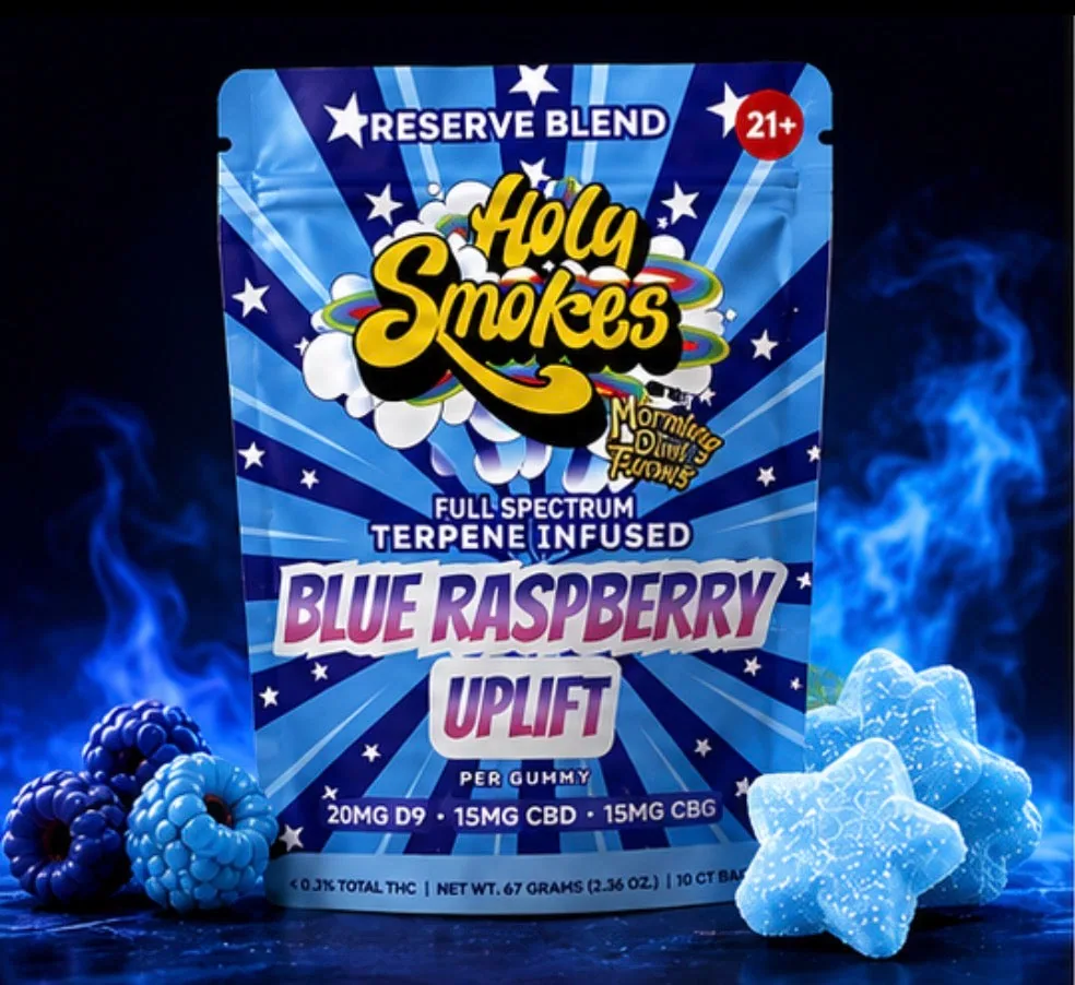 The Blue Raspberry pouch standing in blue smoke, with three star gummies to the right and blue and dark berries to the left.