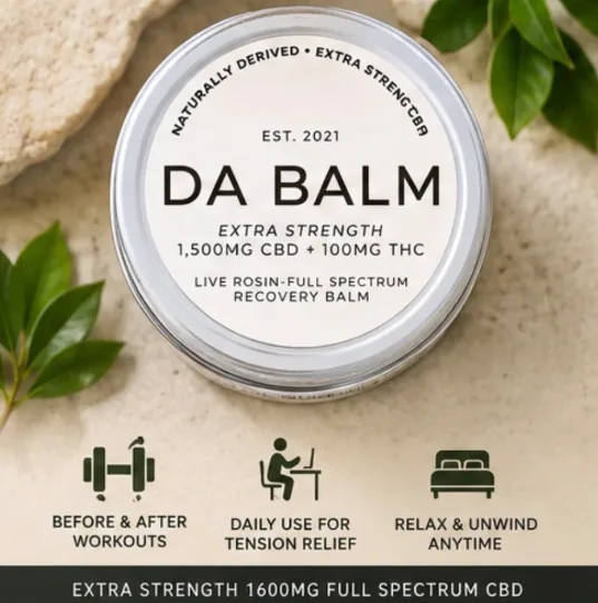 A straight-down shot of the jar's silver lid with its cream printed label facing the camera, lying on a sandy beige surface beside glossy green leaves and a chunk of pale stone. Three small icons sit along the bottom edge.