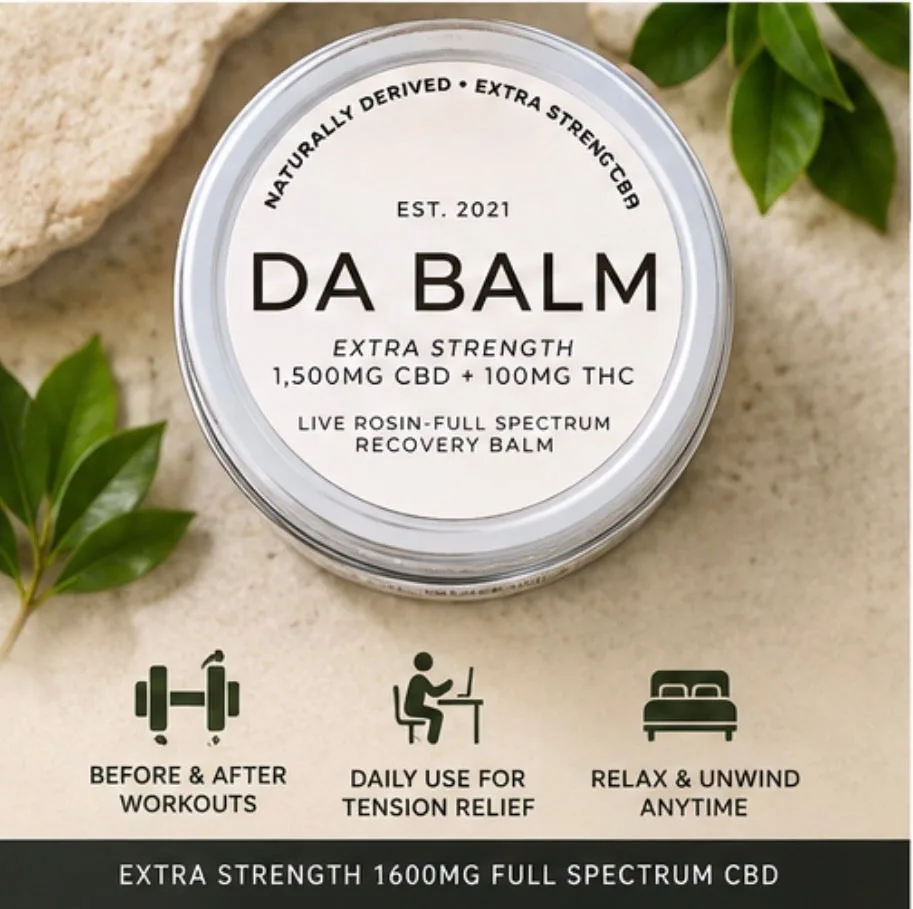 An overhead flat-lay of the closed jar, silver rim catching the light around a cream circular label that reads est. 2021 and lists 1,500mg CBD and 100mg THC. It sits on a pale sandy surface with green leaves at the left and top corners and a piece of textured stone behind.