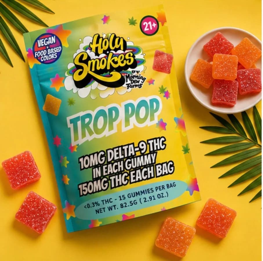 The Trop Pop pouch flat on a yellow background beside a plate of orange gummies and palm leaves.