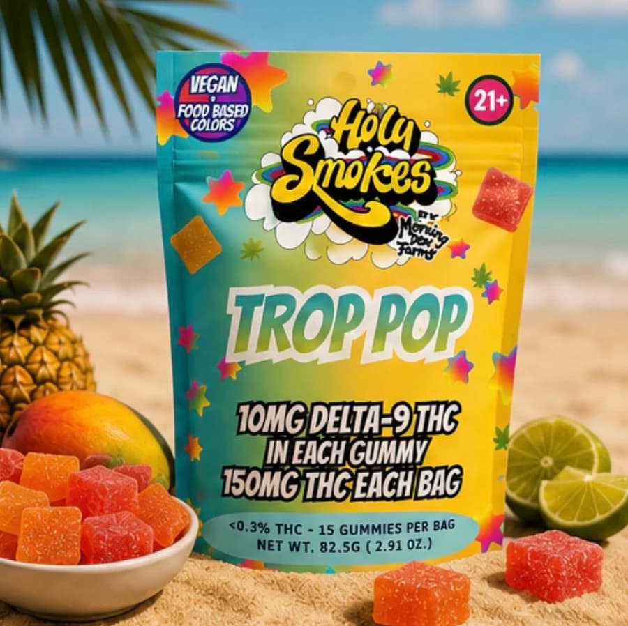 The Trop Pop pouch on a beach backdrop with pineapple and mango, orange gummies scattered in front.