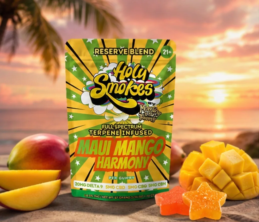 The Maui Mango pouch standing on sand at sunset with palm fronds overhead, mango slices to the left and star gummies to the right.