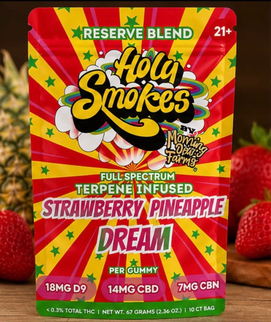 A straight-on shot of the pouch front showing the Holy Smokes logo and the 18mg D9, 14mg CBD and 7mg CBN panel, with strawberries and a pineapple behind it.