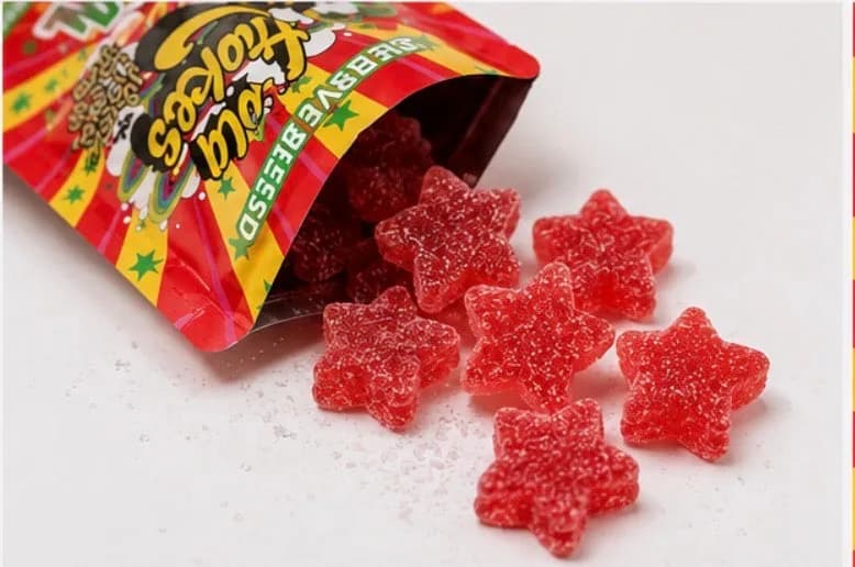 An open pouch lying on a white surface with seven sugared red star gummies spilling out of it.